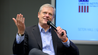 A white male holding a mic speaking while seated