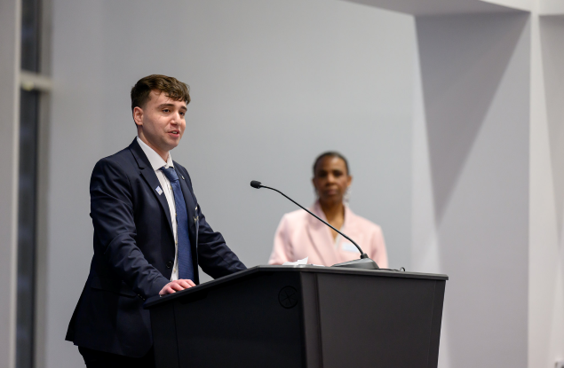 White male student at lectern with black woman looking at him