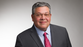 A bespectacled man wearing a red tie and suit