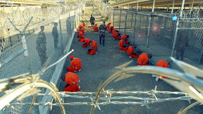 detainees in organge jumpsuits crouching down on the ground