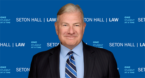 Man in suit and tie in front of a Seton Hall Law step and repeat banner.