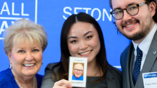 An Asian woman smiling between two white people holding a photo