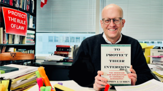 Bespectacled bold white man smiling and holding a book