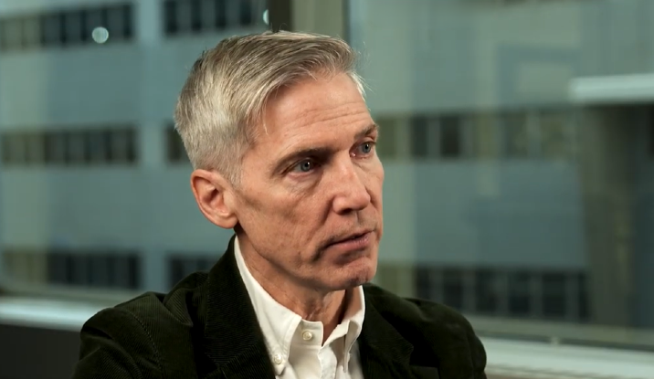 A white man in front of glass window
