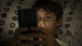 A young person laying in bed using a mobile device.