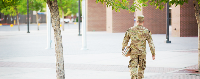 Military man walking with books.