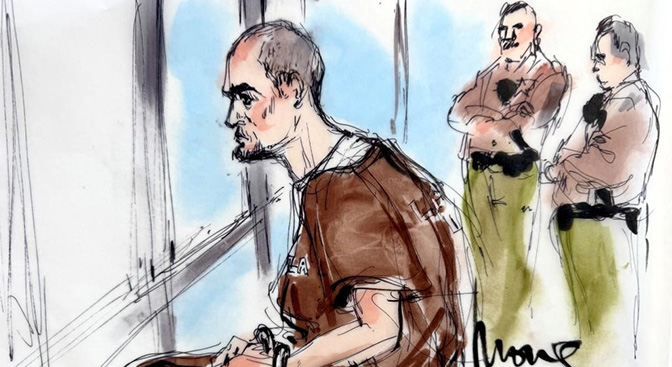 Two men standing behind man seated in brown jumpsuit